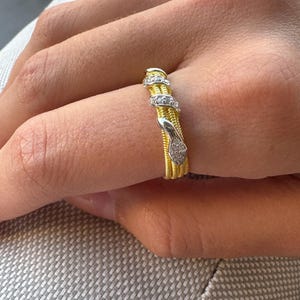Peut inclure: Une bague dorée présentant un motif de serpent enroulé qui entoure le doigt. Le corps du serpent est réalisé avec une finition texturée rappelant une corde et est orné de petites pierres claires incrustées sur la tête et le corps.