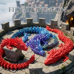 Op de afbeelding: Drie beweegbare fidget-drakenfiguren op een stenen platform. Twee draken zijn effen matrood, terwijl de middelste draak een metallic, iriserende blauwe en paarse afwerking heeft. De tekst FIDGET DRAGON staat boven de figuren.