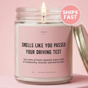 May include: A 9 oz scented candle in a clear glass jar with a metal lid. The label is light pink with black text that reads: LUNARA, SMELLS LIKE YOU PASSED YOUR DRIVING TEST, Top notes of fresh asphalt, base notes of roadworthy, license-earned triumph.