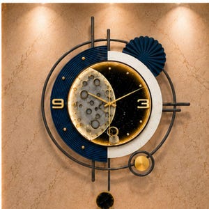 Puede incluir: Un reloj de pared circular con un diseño dividido en una sección azul oscuro acanalada y una sección blanca lisa. El centro muestra una superficie texturizada similar a la luna y un fondo negro estrellado con manecillas doradas, los números 9 y 3, y un péndulo.