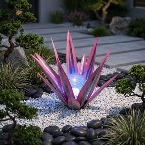 May include: A metal agave plant sculpture featuring pointed, pink-toned leaves with a metallic finish. At the center of the plant sits a spherical, crackled glass light orb that emits a soft, cool-toned blue glow, illuminating the surrounding area.