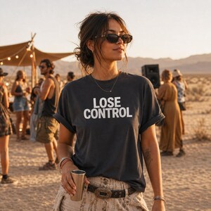 Könnte beinhalten: Ein anthrazitfarbenes Kurzarm-T-Shirt mit dem weißen Schriftzug LOSE CONTROL auf der Brust. Das T-Shirt hat einen Rundhalsausschnitt und hochgekrempelte Ärmel und wird mit einem hellen Gürtel mit auffälliger, dekorativer Metallschnalle kombiniert.