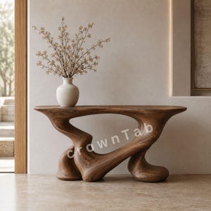 Op de afbeelding: Een bruine houten sidetable met een vloeiende, organische, sculpturale basis en een glad, langwerpig blad. Een witte keramische vaas met delicate, lichtgekleurde gedroogde takken staat op de tafel. De tekst CrownTab is zichtbaar op de tafel.