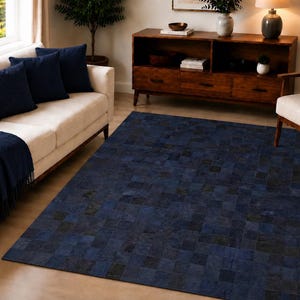 Pode incluir: Um tapete retangular com um design de patchwork composto por pequenas peças quadradas em vários tons de azul-marinho profundo e preto. O tapete tem uma textura plana e uniforme e cobre grande parte do chão da divisão.
