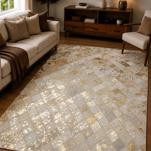 May include: A rectangular area rug featuring a geometric diamond pattern composed of alternating light gray and metallic gold foil-finished panels. The surface displays a mottled, textured appearance across the grid, creating a reflective effect.