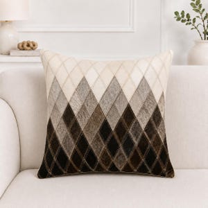 May include: A square throw pillow featuring a diamond argyle pattern. The design transitions from light cream at the top to dark brown at the bottom, with each diamond segment displaying a textured, hair-on-hide appearance with visible stitching.