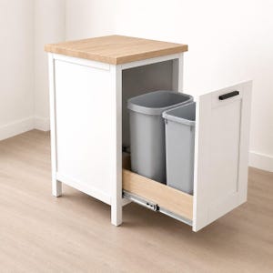 May include: A white kitchen cabinet with a light wood-toned top surface and a pull-out drawer containing two removable grey plastic waste bins. The drawer features a black horizontal handle and is mounted on metal sliding tracks for access.