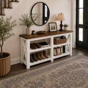 May include: A white wooden console table with a dark brown wood top, featuring two open shelves for storage. The table holds various items including shoes, a woven basket, a bag, a lamp, a framed picture, and a bowl. It has X-shaped side supports.