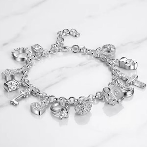 May include: A silver charm bracelet featuring various dangling charms including a star, a key, a heart, a ring with a clear stone, a textured sphere, a cube with a clear stone, a crescent moon, a cross, and a circular ring-shaped charm.