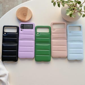 Può includere: Cinque custodie pieghevoli per telefono con una texture trapuntata stile piumino. Le custodie sono disponibili in nero, lavanda, verde, rosa chiaro e azzurro. Ogni custodia presenta un ritaglio rettangolare per la fotocamera e cuciture.