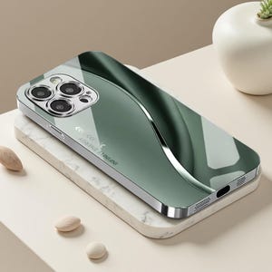 Op de afbeelding: Een donkergroen smartphonehoesje met een glanzende, reflecterende afwerking en een gebogen zilveren accentlijn. Het hoesje heeft een uitsparing voor de drievoudige camera en de tekst "INFINITE ENERGY" in het wit gedrukt aan de zijkant.