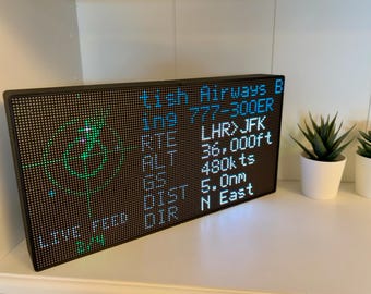 May include: A rectangular black LED pixel display board showing flight data including British Airways B, 777-300ER, LHR to JFK route, 36,000ft altitude, 480kts ground speed, 5.0nm distance, and North East direction with a green radar graphic.