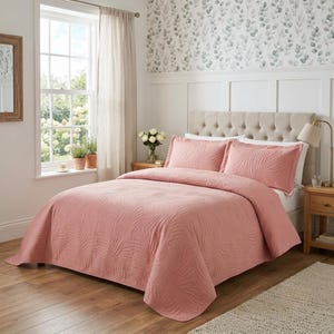 May include: A dusty rose quilt set featuring a textured, embossed palm leaf pattern. The bedding includes a matching bedspread and two rectangular pillow shams, all in a solid muted pink colour, displayed on a tufted beige upholstered headboard.