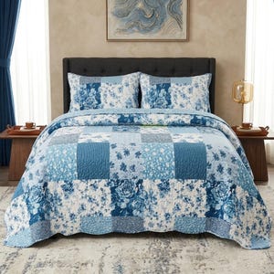May include: A bed featuring a quilt and two matching pillow shams with a blue and white patchwork design. The pattern consists of alternating squares displaying various floral motifs, rose prints, and striped textures in shades of navy and light blue.