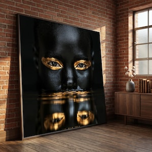 Può includere: Una grande stampa artistica rettangolare da parete che presenta un ritratto in primo piano di una persona con pelle nera profonda e ombretto dorato metallizzato. Il soggetto è posizionato sopra una superficie scura e riflettente.