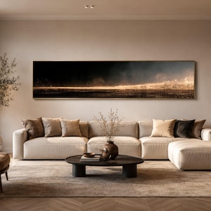 Könnte beinhalten: Ein langes, horizontales, rechteckiges Wandbild, das eine dunkle, atmosphärische Landschaft mit einer leuchtenden, goldenen Horizontlinie zeigt. Das Kunstwerk ist in einem dünnen Metallrahmen gefasst und hängt über einem großen, beigen Sofa.