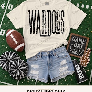 May include: A cream-colored short-sleeve t-shirt with the black text WAR DOGS, blue denim distressed shorts, a brown football, two black and white pom-poms, a small chalkboard with GAME DAY text, a foam finger, and a black megaphone.