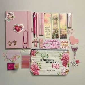 May include: A pink journal, a pencil case with floral patterns and the text God is within her, she will not fall, Psalm 46:5, pens, highlighters, bookmarks with floral designs, stickers, paper clips, and sticky notes in various shades of pink.