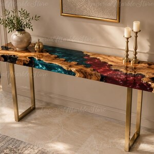 May include: A rectangular console table featuring a natural live-edge wood slab with a central river design made of translucent teal and deep red resin. The table is supported by two brushed gold metal U-shaped legs, creating a sleek and modern look.