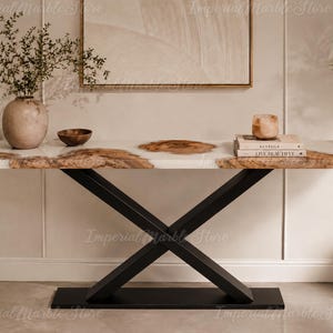 Può includere: Un tavolo console con un piano rettangolare in resina bianca con sezioni di venature del legno naturale incorporate. Il tavolo è sostenuto da una base in metallo nero con un design a croce a X e una piastra rettangolare piatta a terra.