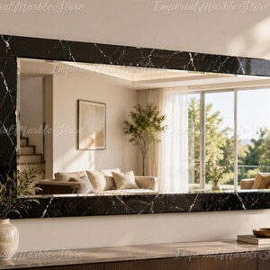 May include: A large rectangular wall mirror featuring a thick frame with a black marble finish and white veining. The mirror surface reflects a bright living room interior with a sofa, a potted plant, and large windows with natural daylight.