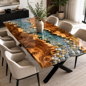 Könnte beinhalten: Ein rechteckiger Esstisch mit einer Massivholzplatte mit Naturkante und einem zentralen, flussartigen Inlay aus blauem Harz, das mit glatten, bunten Flusskieseln gefüllt ist. Der Tisch steht auf einem schwarzen X-förmigen Metallgestell und sechs beigen Stühlen.