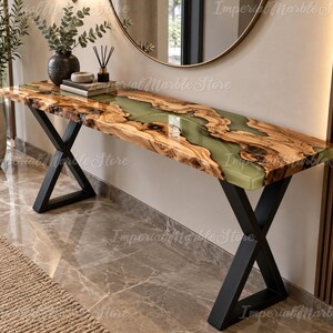 Può includere: Un tavolo console rettangolare caratterizzato da un bordo in legno naturale con un inserto centrale in resina verde salvia traslucida. Il tavolo è sostenuto da due gambe in metallo nero a forma di X. Le venature del legno sono visibili.