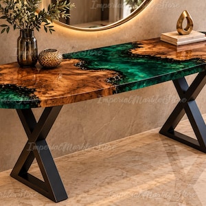 Può includere: Un tavolo console ovale con bordo in legno naturale e un inserto in resina verde smeraldo lucido. Il piano del tavolo è sostenuto da due gambe in metallo nero a forma di X. La superficie presenta venature del legno naturali e una finitura.