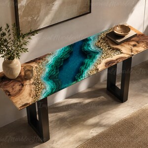 May include: A rectangular console table featuring a natural wood slab top with a central river design made of blue and green resin, accented by embedded light-colored stones. The table is supported by two black metal U-shaped legs.