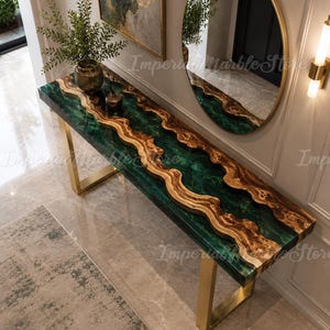 Puede incluir: Una mesa consola rectangular con un centro de madera de borde natural flanqueado por secciones de resina verde oscuro. La mesa está sostenida por dos patas de metal dorado en forma de U. La superficie muestra un patrón de veta de madera ondulada que contrasta con el acabado de resina verde suave y translúcida.