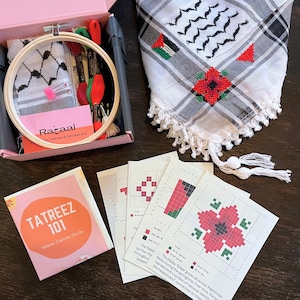 May include: An embroidery kit with a wooden hoop, needles, and threads in a pink box. A black and white checkered scarf with red poppy embroidery and a guide titled "TATREEZ 101" are also present.