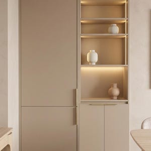 May include: A tall, matte beige cabinet unit featuring a full-length door on the left and a lower double-door cabinet on the right. Above the lower cabinet are three open shelves with integrated vertical lighting, displaying three ceramic vases.