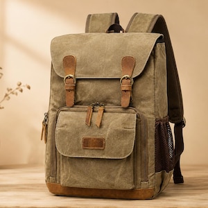 May include: An olive green canvas backpack featuring a top flap with two brown leather straps and brass buckles. The bag includes a front zippered pocket with a leather patch, side mesh pockets, and adjustable shoulder straps with brown leather accents.