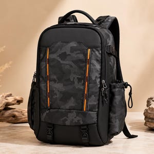 Pode incluir: Uma mochila preta com um padrão de camuflagem cinza-escuro no painel frontal. A bolsa inclui duas faixas refletoras laranja verticais, bolsos laterais com fecho de cordão e duas fivelas de plástico preto na base.