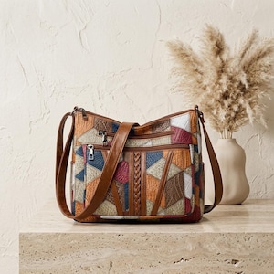 Puede incluir: Un bolso de hombro de patchwork multicolor con un patrón geométrico texturizado en tonos marrón, azul, rojo y blanco. El bolso incluye una correa de aspecto de cuero marrón, dos bolsillos frontales con cremallera y un detalle trenzado vertical.