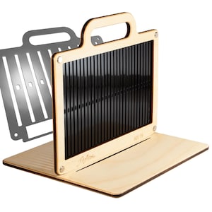 May include: A light-colored wooden loom tool with a handle and a black vertical-slotted insert. The frame features metal corner fasteners and the text "AH 15" and a script logo. A separate silver-colored metal plate with vertical slots is visible.
