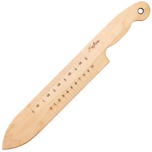 May include: A light-colored wooden tool shaped like a knife with a pointed tip and a handle featuring a circular hole. The blade is marked with two parallel scales, one showing measurements in inches from 0 to 5 and another from 0 to 10.