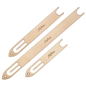 May include: Three light-colored wooden weaving shuttles of varying lengths, each featuring a pointed end with a circular hole, a central slot, and a U-shaped notch at the opposite end. The brand name Sujua is engraved on the surface of each tool.