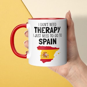 May include: A white ceramic mug with a red handle and rim. The front features the black text I DON'T NEED THERAPY I JUST NEED TO GO TO SPAIN above a graphic of the map of Spain filled with the red and yellow colours of the Spanish national flag.