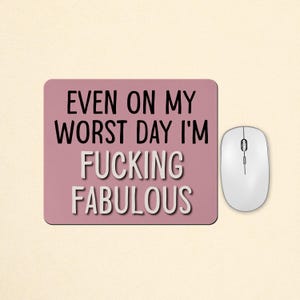 May include: A rectangular mauve mouse pad featuring the black text EVEN ON MY WORST DAY I'M and the white text FUCKING FABULOUS, positioned next to a white computer mouse. The design is centred on the pad with a clean, bold sans-serif font.