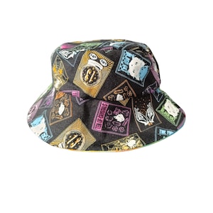 May include: A black bucket hat with a colorful pattern of tarot cards. The cards feature various symbols and imagery, including the Ten of Crystals, the Eight of Swords, and the Three of Wands.