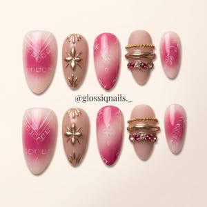 Puede incluir: Un juego de diez uñas postizas en forma de almendra con un diseño degradado en rosa y nude, patrones geométricos blancos, detalles florales dorados y bandas horizontales de cuentas doradas y pedrería rosa. El texto dice @glossiqnails._