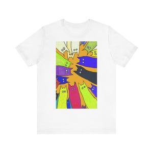 Puede incluir: Una camiseta blanca de manga corta con un estampado gráfico rectangular en el pecho. El estampado muestra una colección de ilustraciones de gatos estilizadas y coloridas en tonos azul, verde, amarillo, rosa, morado y negro sobre un fondo naranja.