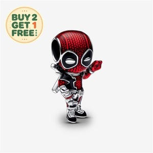 Puede incluir: Un pequeño dije de metal con forma de personaje estilizado con un traje texturizado en rojo y negro, parches blancos en los ojos y una mano levantada. El dije presenta un acabado brillante y detalles intrincados en la cabeza, el torso y las botas.