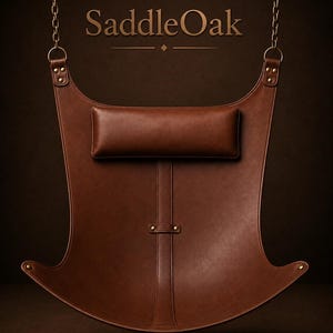 May include: A brown leather hanging chair with a rectangular headrest, vertical strap, and brass-colored metal rivets. The chair is suspended by two metal chains attached to the top corners. The text SaddleOak is printed in gold above the chair.