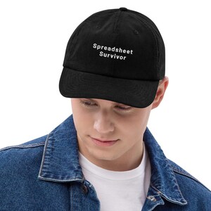 Peut inclure: Une casquette de baseball noire avec le texte brodé en blanc Spreadsheet Survivor sur le panneau avant. La casquette présente une visière incurvée et une calotte structurée, fabriquée dans un tissu noir uni avec des coutures visibles.