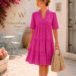 May include: A vibrant magenta knee-length dress featuring an intricate eyelet lace pattern, a V-neckline, and short sleeves. The dress has a tiered skirt design and is paired with a beige woven straw handbag with a tassel detail.