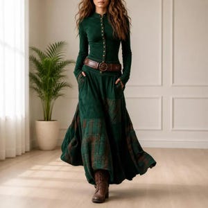 May include: A long-sleeved dark green dress featuring a button-down bodice, a brown leather belt at the waist, and a floor-length skirt with a dark green and brown plaid pattern on the lower section. The dress is paired with brown leather boots.