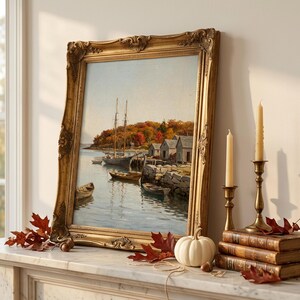 May include: A framed oil painting depicting a harbor scene with sailboats, small wooden rowboats, and coastal buildings nestled against a backdrop of autumn foliage. The artwork is encased in an ornate, antique-style gold frame with intricate detailing.