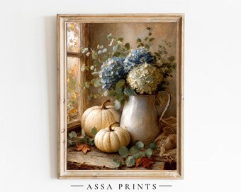 May include: A framed wall art print featuring a still life painting of blue and white hydrangea flowers in a light-colored ceramic pitcher, accompanied by two pale pumpkins and green foliage on a wooden surface near a window. Text reads ASSA PRINTS.
